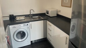 A compact kitchen with a washing machine, a microwave, a sink, and a stainless steel refrigerator.