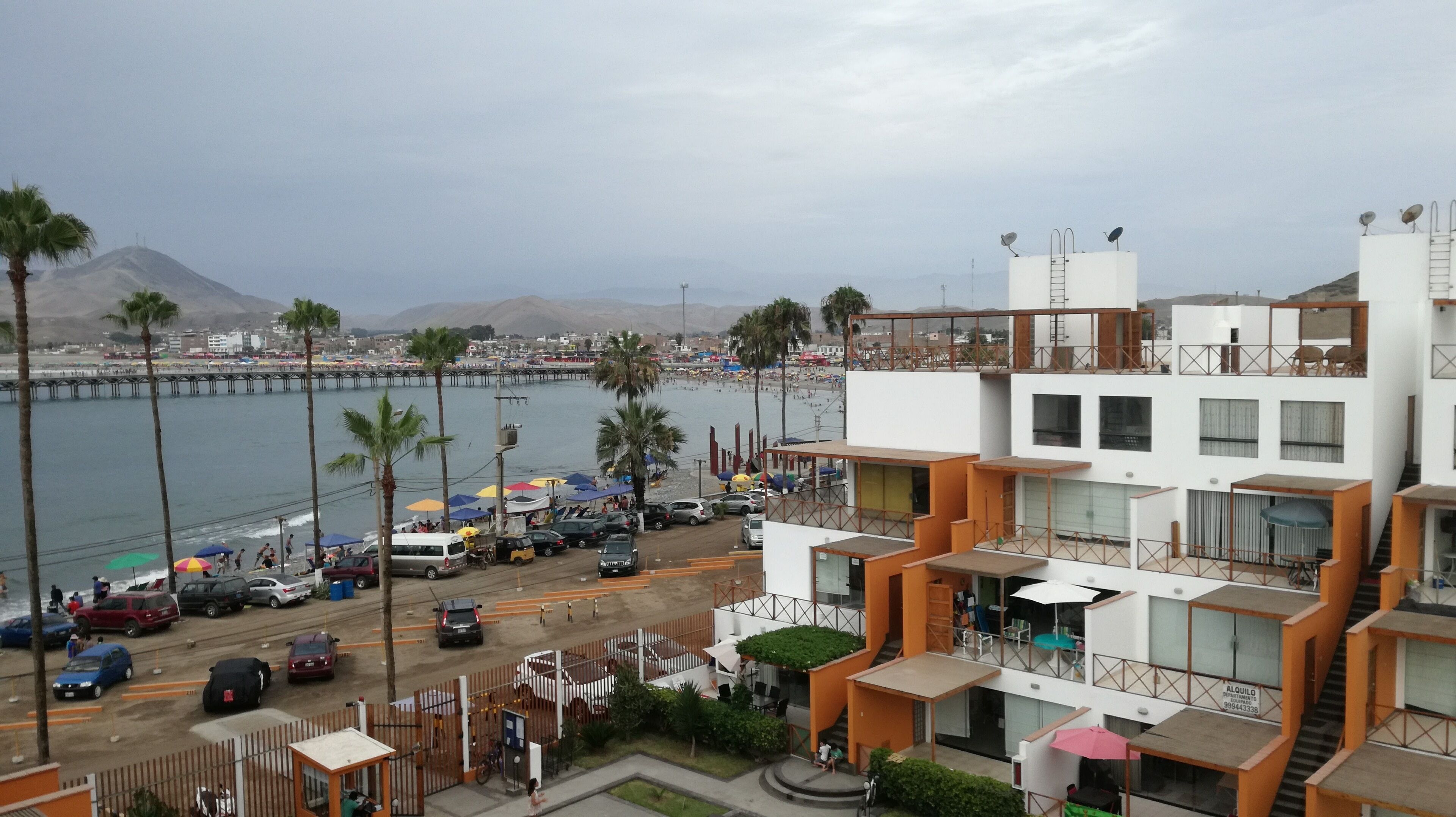 Ein Küstengebäude mit mehreren Balkonen, Blick auf den Strand und einem Pier im Hintergrund.