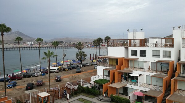 A coastal building with multiple balconies, a view of the beach, and a pier in the background.