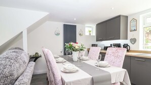 A modern dining area with a long table set for four, flanked by cushioned seating. - Lilly's Cottage (Dawlish)