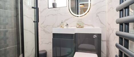 A modern bathroom with a glass shower enclosure, a white toilet, a vanity with a mirror, and marble tiles.
