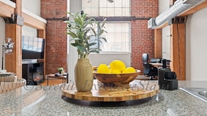 Une cuisine dotée d’un plan de travail en granit, d’un vase contenant des plantes vertes, d’un saladier en bois rempli de citrons et d’un ventilateur de plafond moderne.