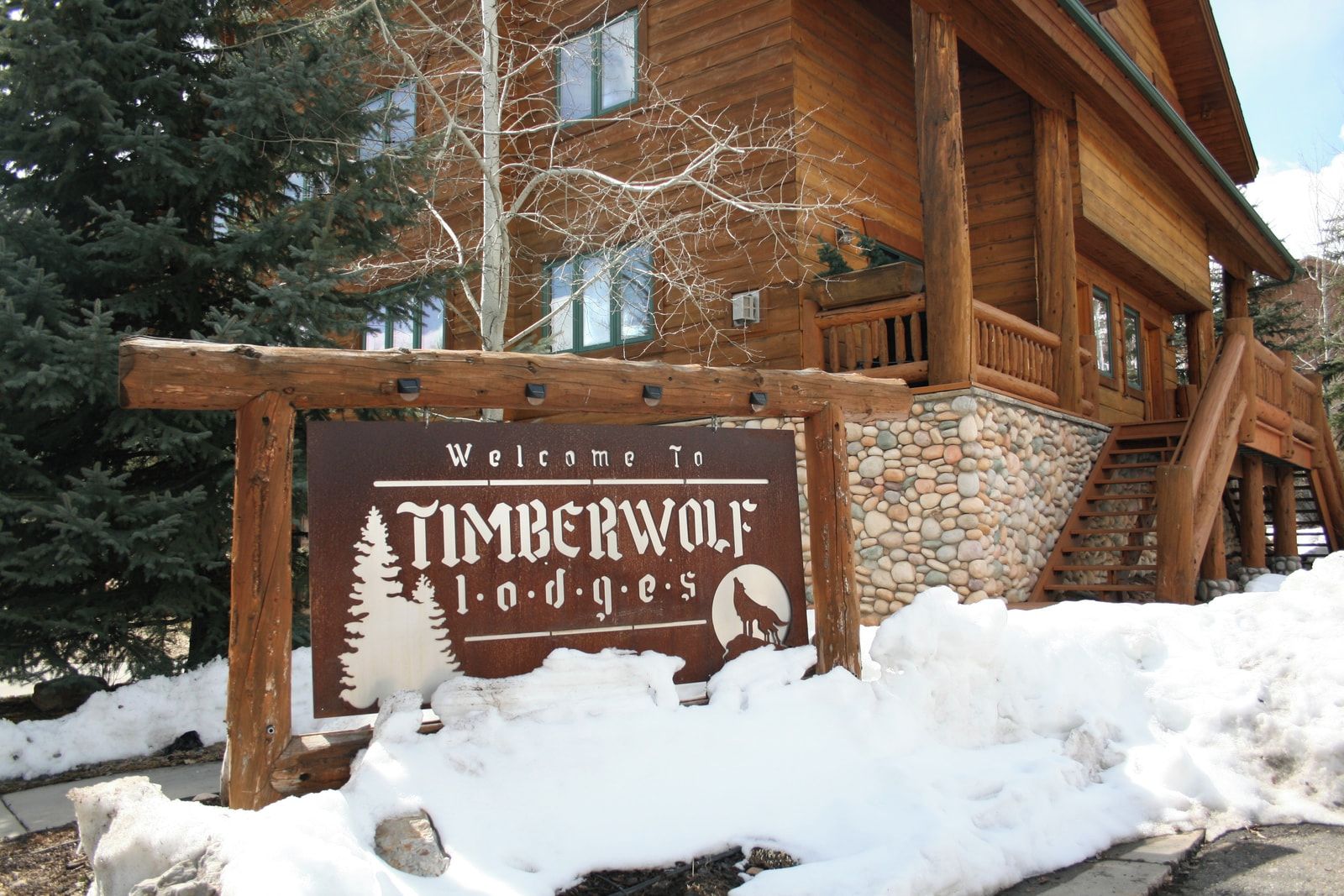 Placa de madeira com silhueta de um lobo e uma árvore, indicando Timberwolf Lodge.