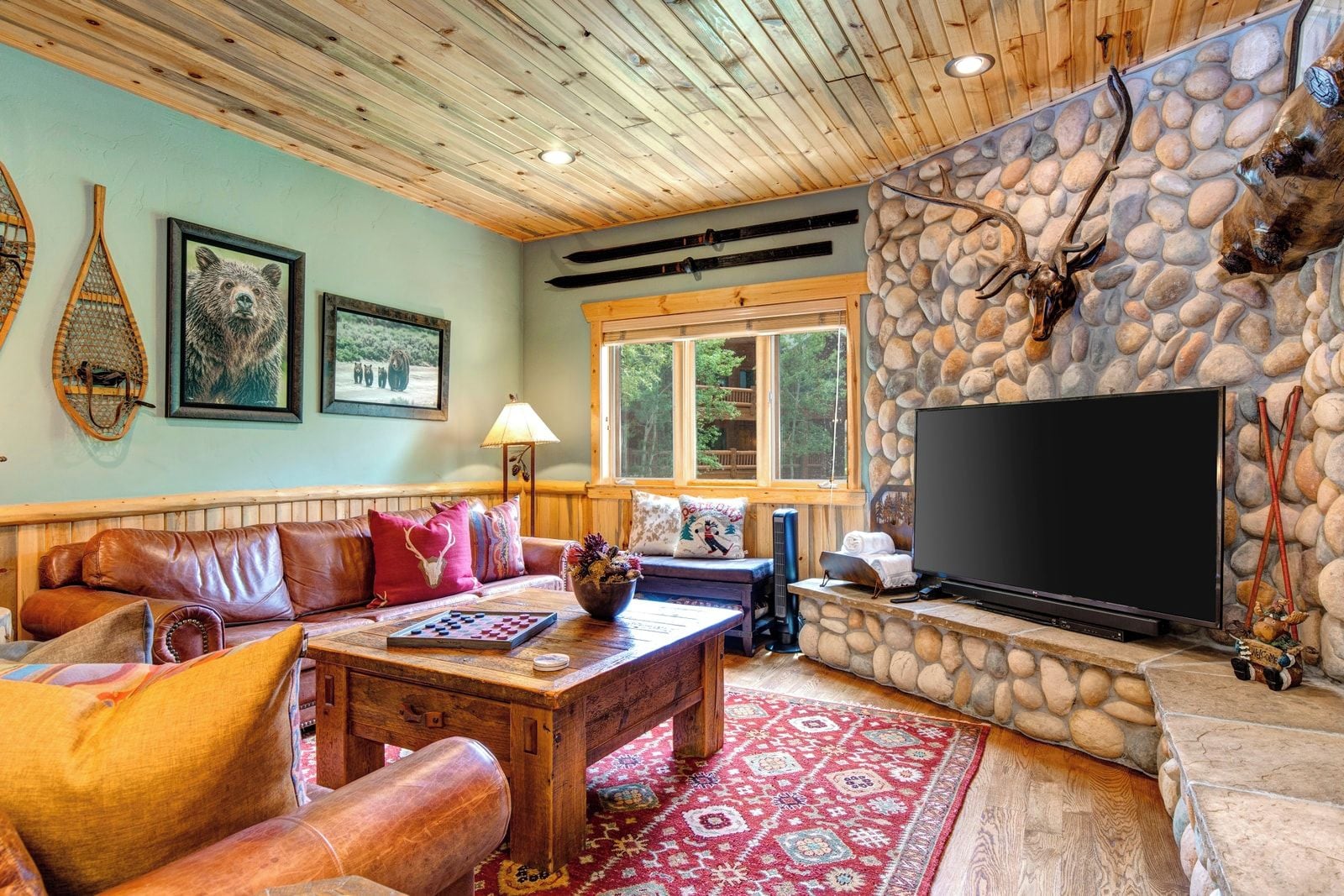 A cozy living room with a stone fireplace, a large flat-screen TV, and a wooden ceiling.
