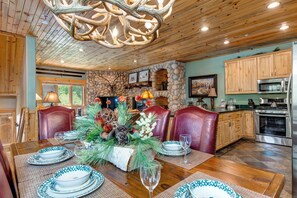 A dining area with a stone fireplace, wooden ceiling, and a chandelier.