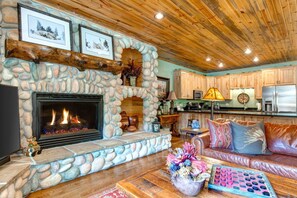 A stone fireplace with a fire, wooden ceiling, kitchen area, and a leather sofa. - Timber Wolf Lodge | KBM Resorts | Gas Fireplace, Common Hot Tubs, Near Canyons Village | 2 Units, 5 Bedrooms | ML-1343 (Park City)