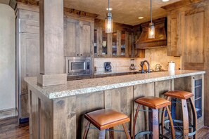 A kitchen with a granite countertop, wooden cabinets, a stainless steel microwave, and a bar stool.