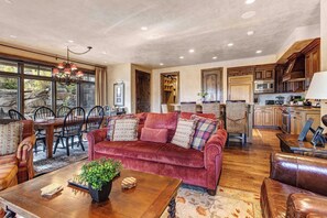 A spacious living room with a red velvet sofa, a dining area with a wooden table and chairs, and a kitchen with wooden cabinets.