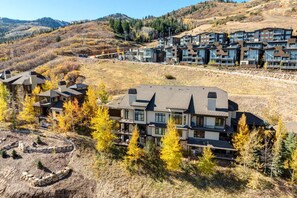 A modern resort with multiple buildings, featuring a mix of residential and commercial spaces, set against a backdrop of autumnal trees and hilly terrain.
