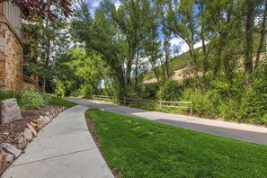 A paved pathway flanked by lush greenery and a stone building.