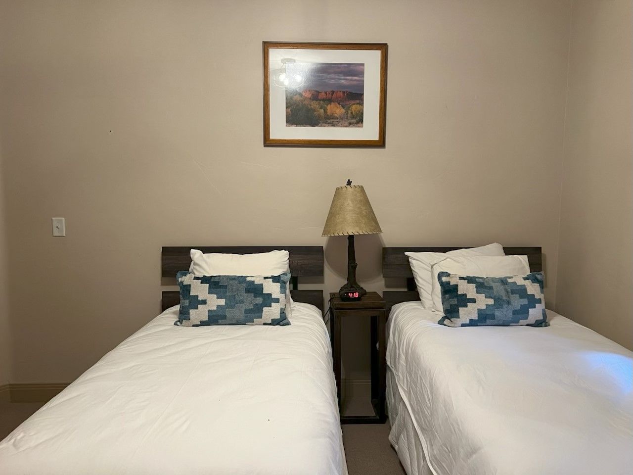 Camera d'albergo con due letti, un comodino con una lampada e un quadro appeso al muro.
