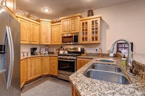 A kitchen with wooden cabinets, a stainless steel refrigerator, a microwave, an oven, granite countertops, and a sink with a faucet.
