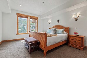 A bedroom with a wooden bed, two bedside lamps, a nightstand, a bench, and a window with a view. - Town Pointe | KBM Resorts | Walk To Town, Common Elev | 2 Units, 6 Bedrooms | ML-1347 (Park City)