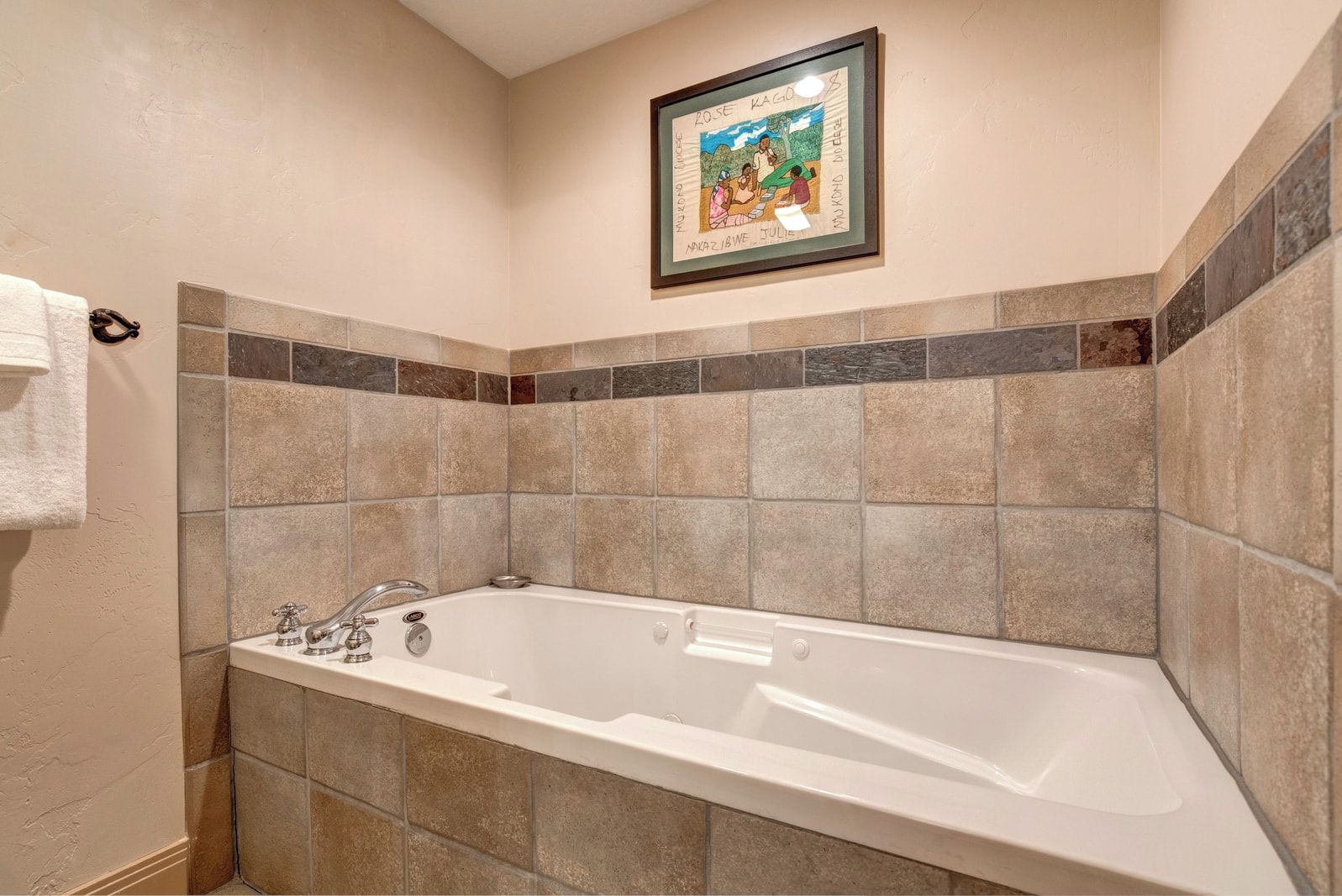 Un baño con bañera, paredes con azulejos y un cuadro enmarcado en la pared.