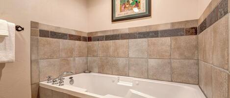 Un baño con bañera, paredes con azulejos y un cuadro enmarcado en la pared.
