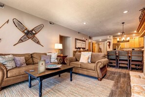 A living room with a sofa, coffee table, and a dining area with wooden chairs and a kitchen in the background. - Town Pointe | KBM Resorts | Walk To Town, Common Elev | 2 Units, 6 Bedrooms | ML-1347 (Park City)