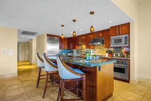 A modern kitchen with a central island, bar stools, stainless steel appliances, and pendant lighting.