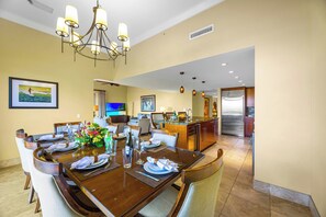 A dining area with a wooden table set for four, a chandelier, and a kitchen in the background.