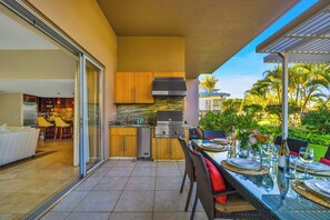 Una cocina moderna con una parrilla empotrada, un comedor con mesa de vidrio y vistas al jardín.