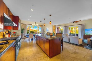 Une cuisine moderne avec un îlot central, un coin repas avec des chaises, un salon avec un canapé et un téléviseur.