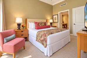 Habitación de hotel con cama, una silla, una mesita de noche, una lámpara y un cuadro en la pared.