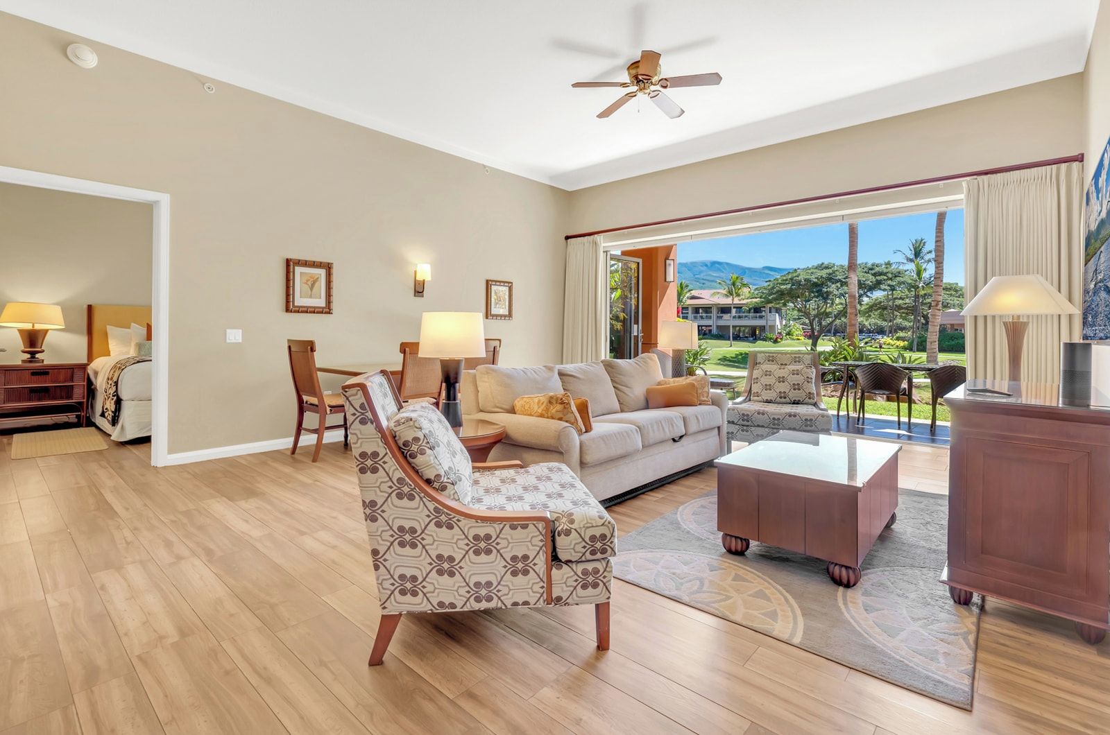 A spacious living room with a sofa, armchairs, a coffee table, and a view of a tropical landscape through large windows.