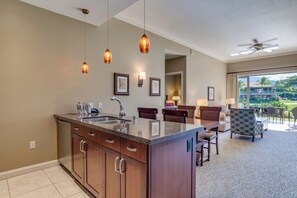 A modern kitchen with a central island, dining area with chairs, and a view of a building and greenery.