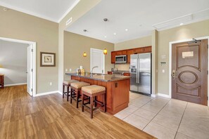 A kitchen with a central island, wooden bar stools, a stainless steel refrigerator, and a microwave.