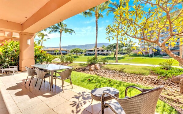 Un espacio al aire libre cubierto con una mesa y sillas, vista a un campo de golf y palmeras.