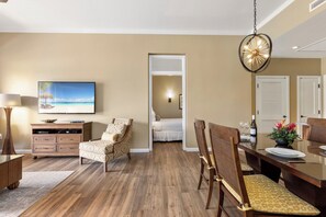 Une chambre d’hôtel avec un plancher en bois, un coin repas avec une table et des chaises, un téléviseur fixé au mur et un lit à l’arrière-plan.