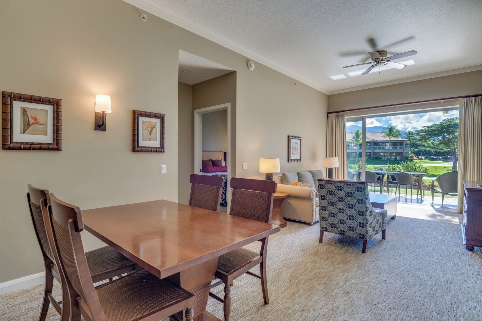 Habitación de hotel con una mesa de comedor, sillas, un sofá, un sillón estampado y vistas al exterior.