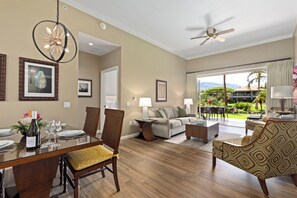 A hotel room with a dining area, a living room with a sofa and coffee table, a ceiling fan, and a view of the outdoors.