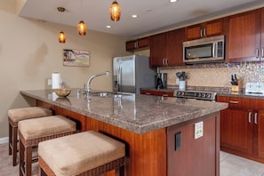 A kitchen with a granite countertop, stainless steel appliances, wooden cabinets, and a hanging light fixture.
