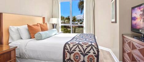 A hotel room with a bed, a TV, a window with curtains, and a view of palm trees.