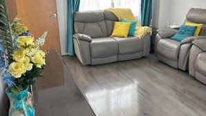 A living room with a grey leather sofa, a yellow vase with flowers, and a wooden floor. - Lavish 3 story house : Double Room with Shared Toilet (Dagenham)