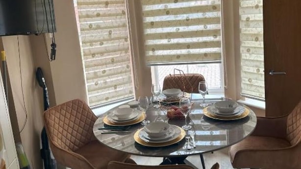 A dining area with a round table set for four, surrounded by cushioned chairs. - Lavish 3 story house : Double Room with Shared Toilet (Dagenham)