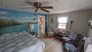 Un dormitorio con cama, ventilador de techo, un mural de un río, una ventana y una silla.