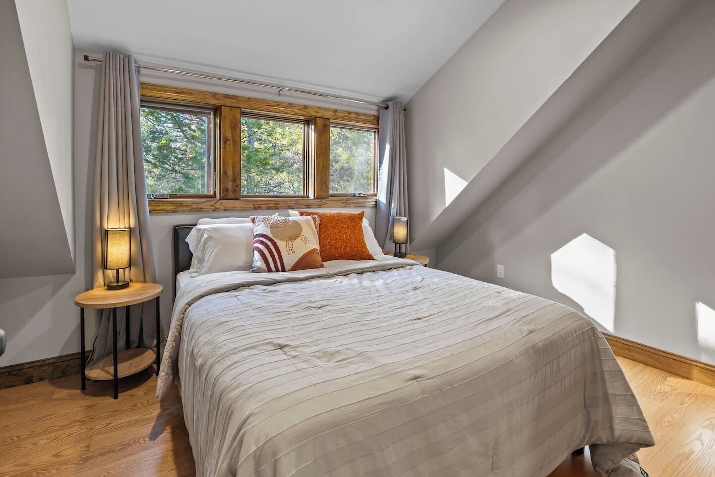 A bedroom with a large bed, two bedside lamps, and a window with curtains.