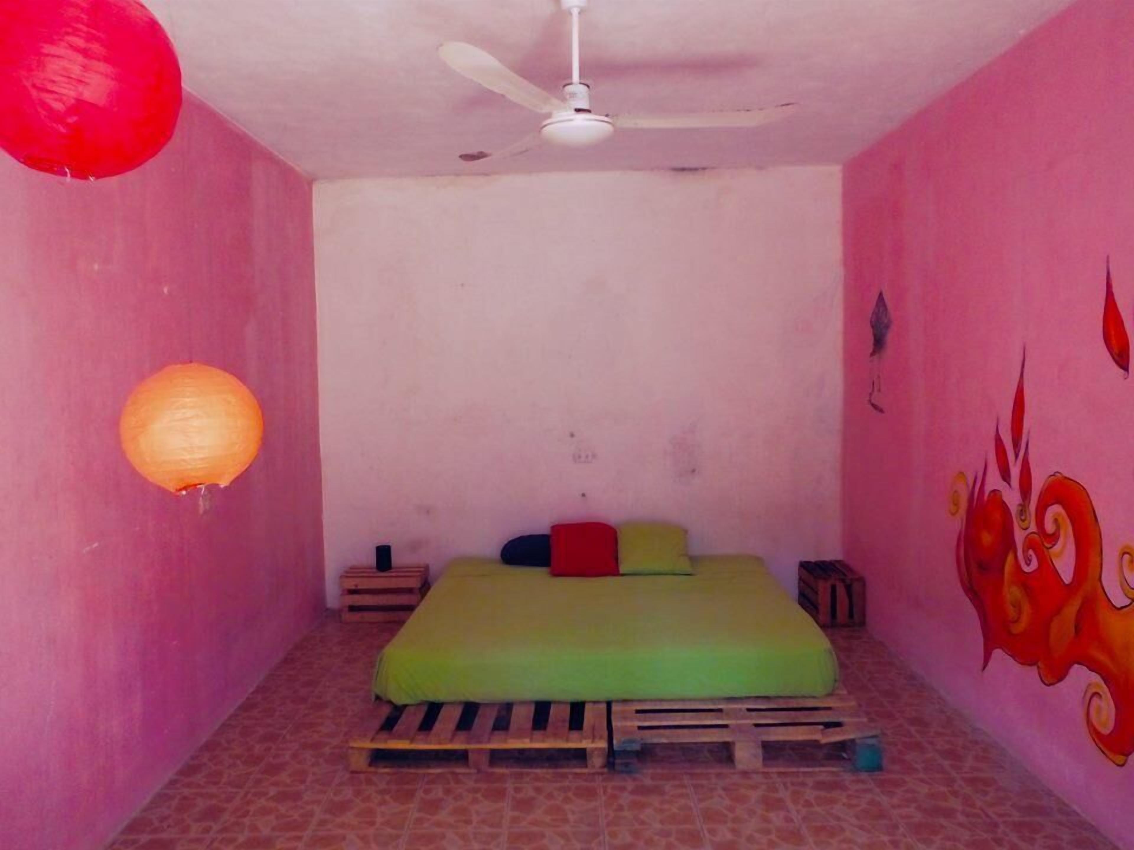 A small room with a single bed, a ceiling fan, and a wall with a colorful mural.
