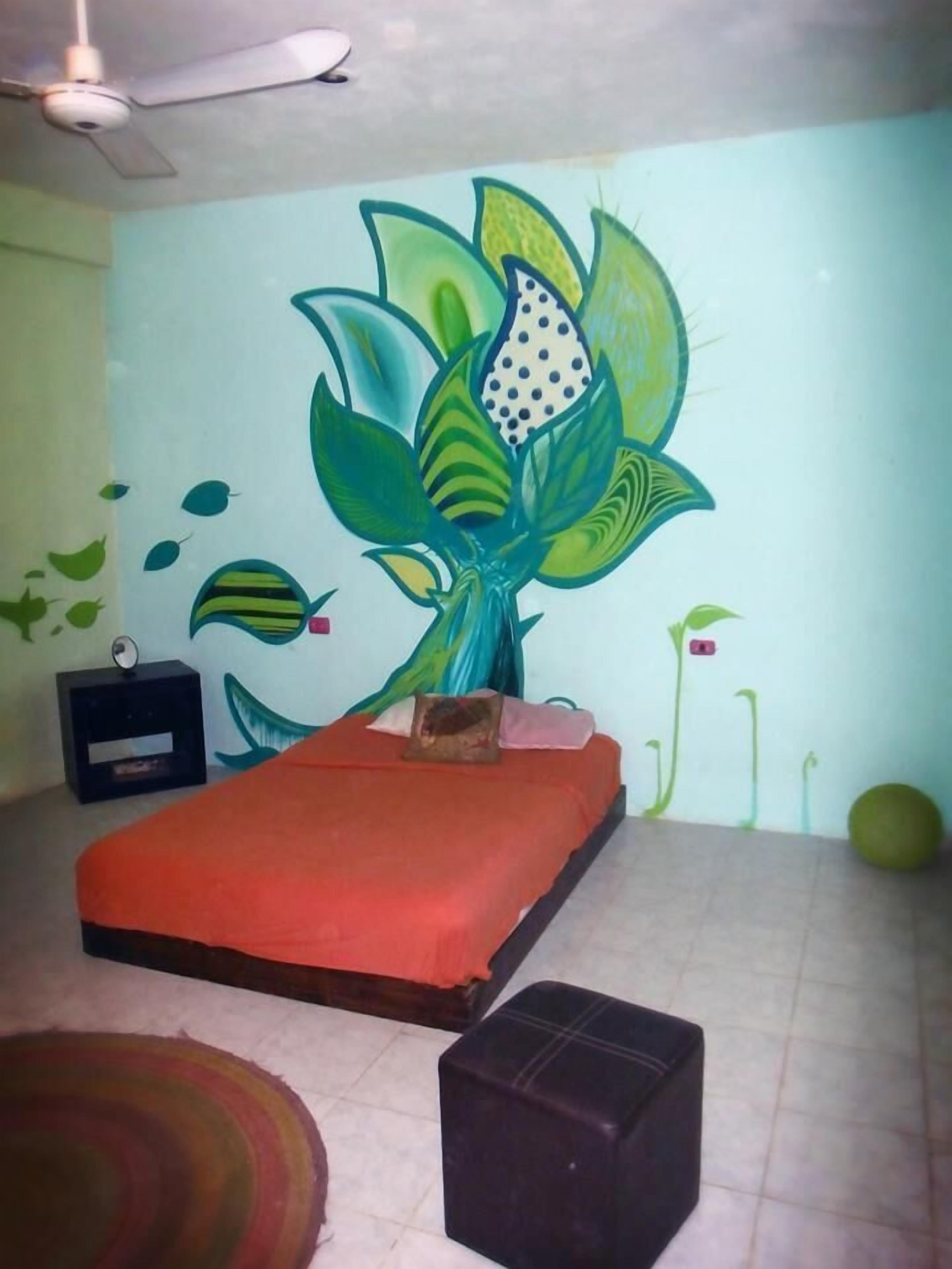 Un dormitorio con cama, mesita de noche, un mural en la pared y ventilador de techo.