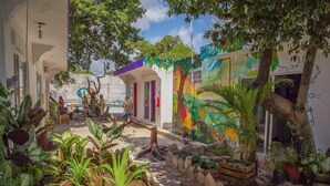 A courtyard with a mural, potted plants, and a tree. - Akadia Hostal Cultural (Tulum)