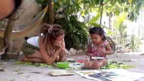 Two people sitting on the ground, surrounded by scattered books and papers. - Akadia Hostal Cultural (Tulum)