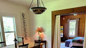 Una habitación acogedora con una mesa de madera, sillas, una lámpara y una cama con una manta colorida.