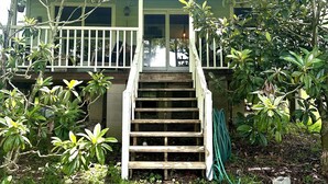 Una casa con porche, una escalera que lleva a la entrada y un jardín con diversas plantas.
