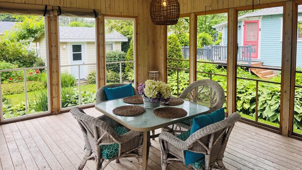 Un patio couvert aménagé avec des meubles en osier, une table en verre et un luminaire suspendu.