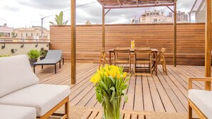Een terras op het dak met houten meubels, een tafel en een vaas met gele bloemen.