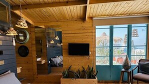 Ein Holzblockhaus-Innenraum mit Bett, Fernseher, Fenster mit Aussicht und einer Pflanze.