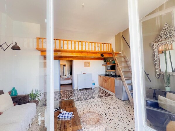 A spacious living area with a high ceiling, a wooden staircase, a kitchen with wooden cabinets, and a patterned floor. - Blue Marlin Batroun (Batroun)