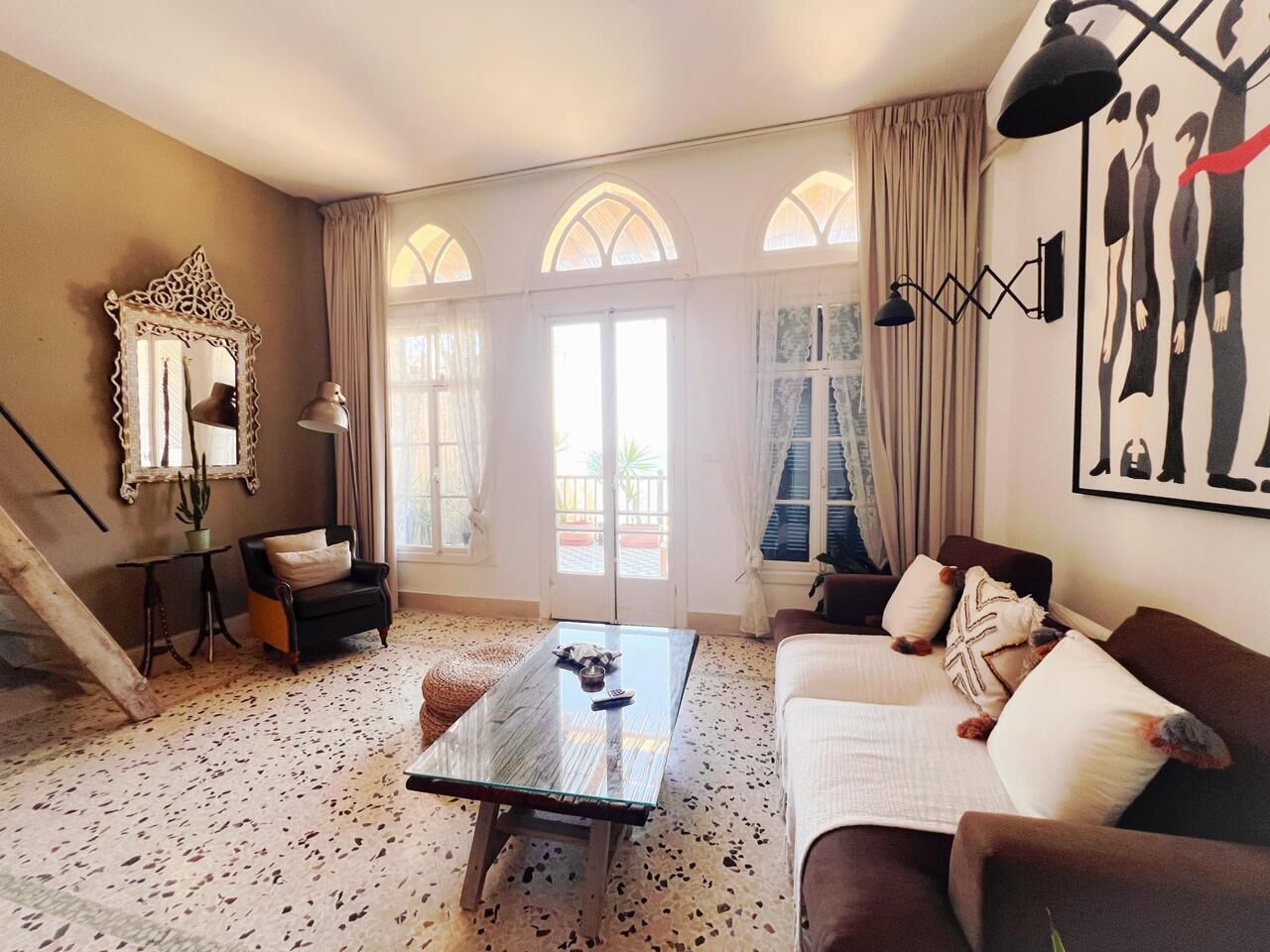 Un salon avec une table en verre, un canapé, un fauteuil, un miroir et une fenêtre avec des rideaux.