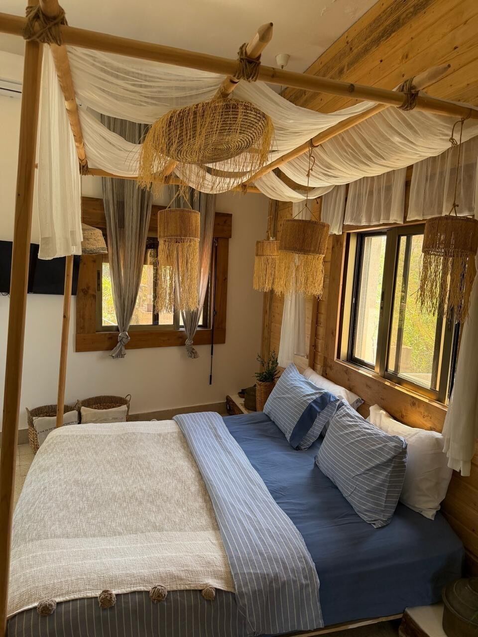 Un dormitorio de cabaña de madera con cama, cestas colgantes y una ventana.